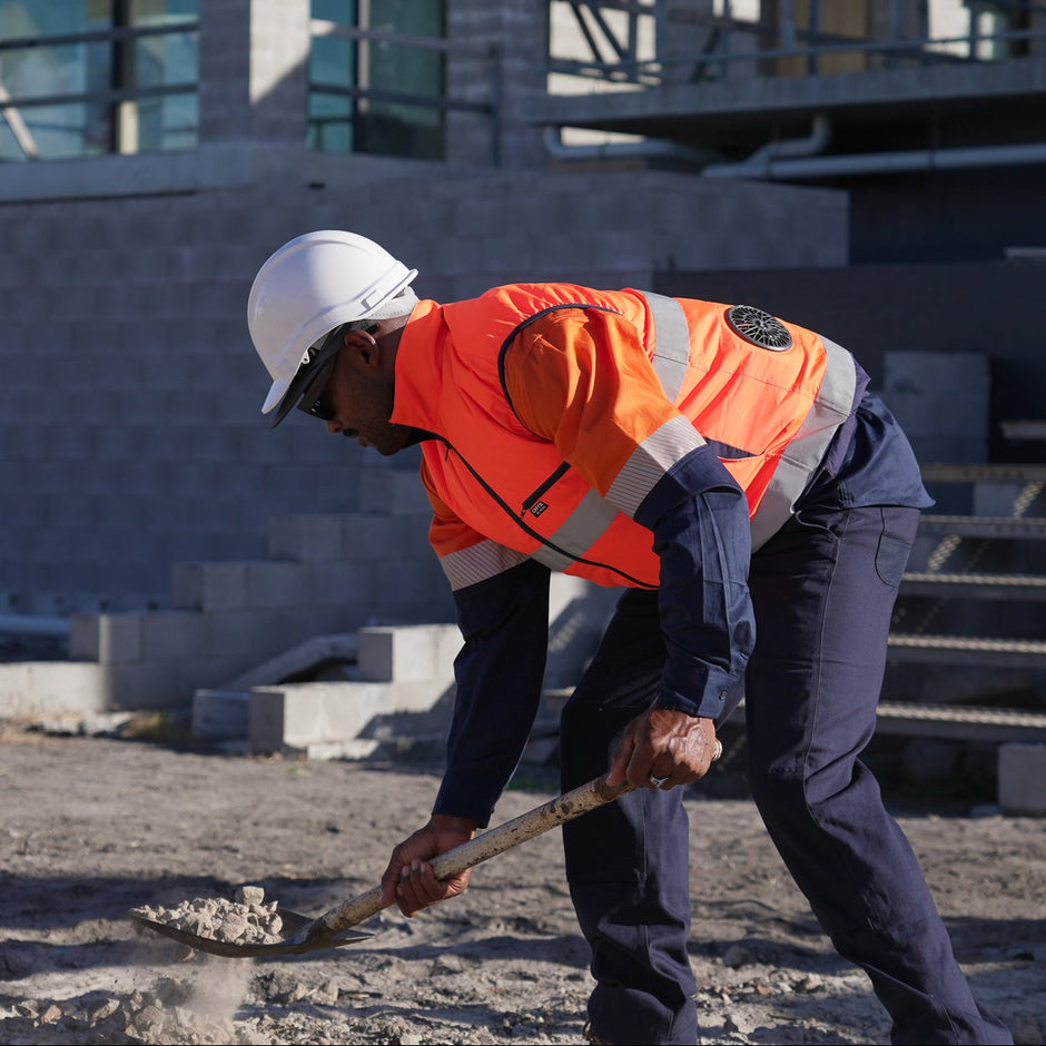 Person in orange safety fan cooled ac wear cooling air conditioned vest and hard hat using a shovel on a construction site.