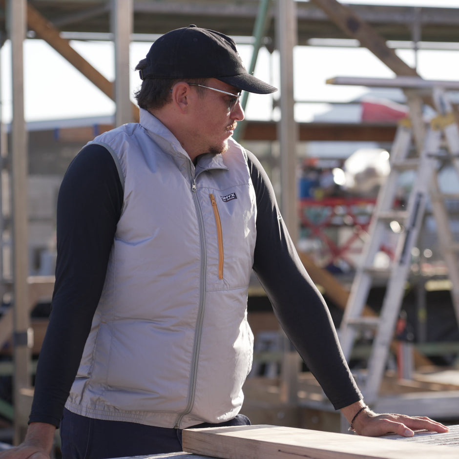 Person wearing a white ac wear fan cooled jacket air conditioned vest with a logo, standing outdoors near construction materials.