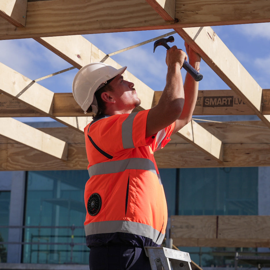 Worker in high-visibility fan cooled jacket ac wear air conditioned workwear cooling vest and hard hat using a hammer on a wooden construction site